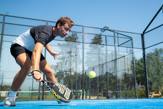 a man is playing padel on a court and using a tecnifibre wall breaker 365 padel racquet receiving a ball